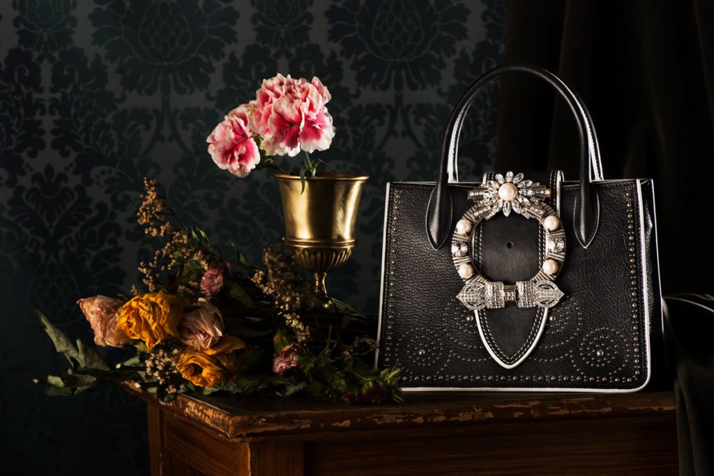 Composizione fotografica stile natura morta con frutta e borsa MIULady. Set design artistico con atmosfera pittorica per accessori lusso